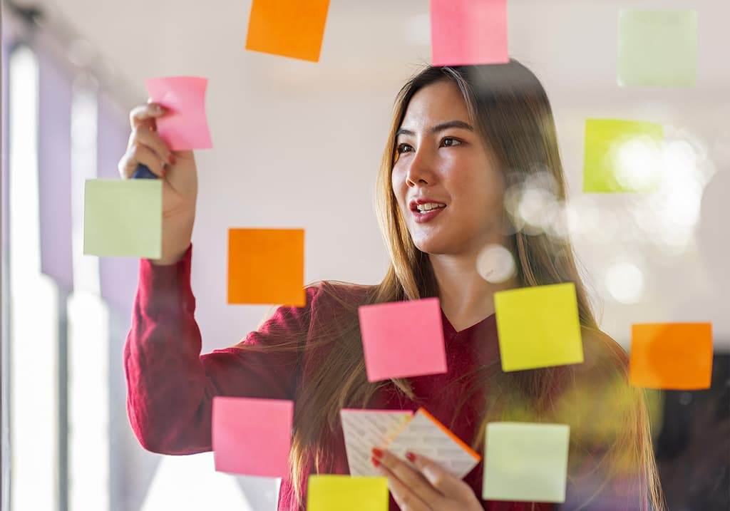 A businesswomen is looking at coloured Post-It notes on a clear wall