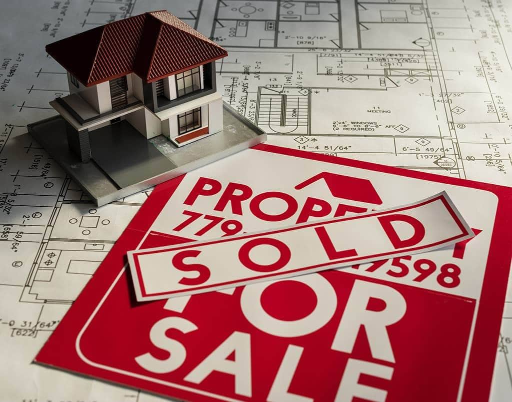 A property sold sign beside a model of a home, on a table covered with blueprints